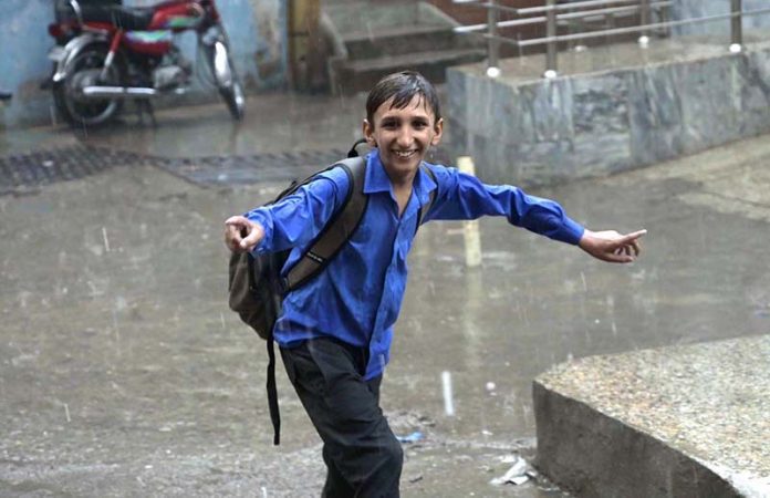 A schoolboy gets drenched while playing and splashing in the season’s first winter rain, celebrating the arrival of the chilly weather