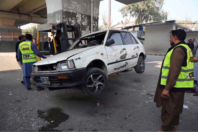 Police officials remove a damaged car from the spot of a suicide attack on the Federal Constabulary headquarters, where three FC soldiers were killed and 11 civilians injured