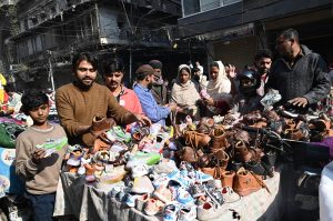 Shoppers browse and purchase shoes from a hand-carried vendor on a holiday in the city