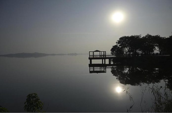 A serene afternoon scene at Rawal Lake in the federal capital, with the sun casting its reflection across the still water near a lakeside viewing platform