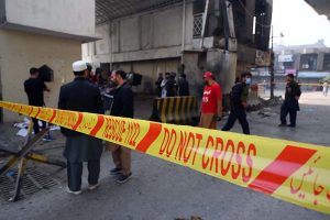 Police officials remove a damaged car from the spot of a suicide attack on the Federal Constabulary headquarters, where three FC soldiers were killed and 11 civilians injured
