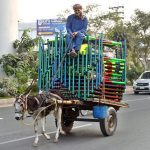 A man rides his donkey cart loaded with Iron bed along Multan Road, heading to deliver them to their destination