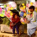 A vendor couple holds colorful light-up balloons to attract customers for selling in Latifabad.