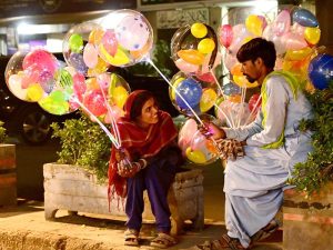 A vendor couple holds colorful light-up balloons to attract customers for selling in Latifabad.