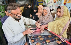 A woman gets her biometric verification done at a mobile shop in a cloth market to avail financial assistance under the Benazir Income Support Programme (BISP).