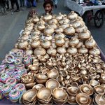 A vendor arranging and displaying the golden color Money Clay pots and oil clay lamps on their handcart at roadside setup in the Provincial Capital
