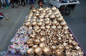 A vendor arranging and displaying the golden color Money Clay pots and oil clay lamps on their handcart at roadside setup in the Provincial Capital