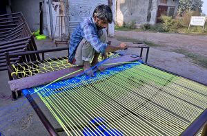 A craftsman skillfully weaves a traditional bed, or ‘charrpai’, using colorful ropes at his workshop.