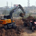 Heavy machinery operates as an excavator lifts soil and loads it onto a tractor-trolley during development and earth-cutting work at Qila Qasim Bagh