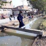 Girl crosses a canal using a temporarily laid electric pole at Shamsher Town