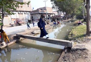 Girl crosses a canal using a temporarily laid electric pole at Shamsher Town