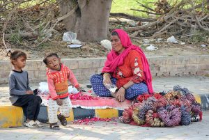 A female vendor with her children waits for customers to sell colorful bangles on the side of the road in the city.
