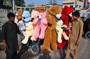 A customer selects a teddy bear from a roadside soft toy stall.