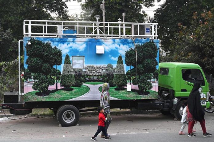 Woman with children walk past a mobile automatic air quality monitoring station parking along a roadside to mentor air quality index in the Provincial Capital