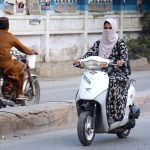 A woman rides a scooty without a helmet, breaching traffic laws, on her way to the office in the city