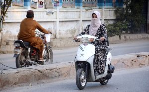 A woman rides a scooty without a helmet, breaching traffic laws, on her way to the office in the city