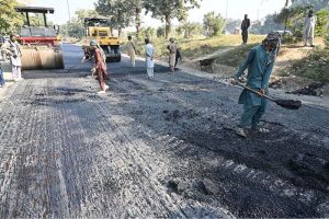 Workers operate a road roller to level and carpet the road with compact gravel on a damaged section as part of ongoing construction work aimed at improving transportation facilities near the IJP Service Road