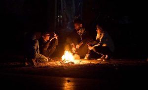 A person sits with children around a fire to keep warm during the cold weather in the Federal Capital.