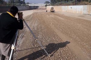 Workers operate a road roller to level and carpet the road with compact gravel on a damaged section as part of ongoing construction work aimed at improving transportation facilities near the IJP Service Road