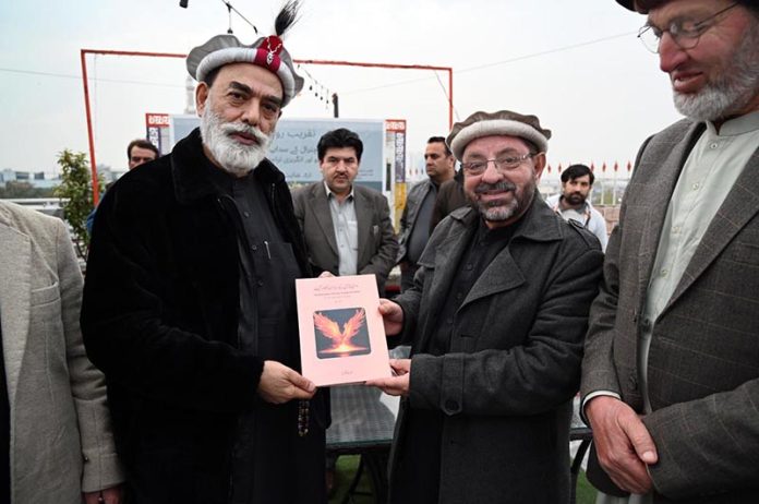 Qazi Inayat Jalil Anbar, a prominent Khowar literature writer, poet, and radio host, presents his book to Senator Talha Mahmood during the ceremony marking the launch of his new book “Sada Bahar Khowar Geet” (Volume I)
