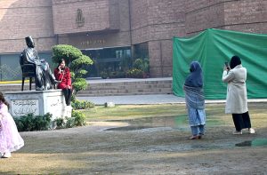 Girls pose and take photos with their mobile phones next to the statue of Dr. Allama Iqbal at Al-Ahmar Hall.