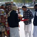 Customers select to purchase colorful handmade household items displayed by a street vendor on the back of his bicycle along a roadside