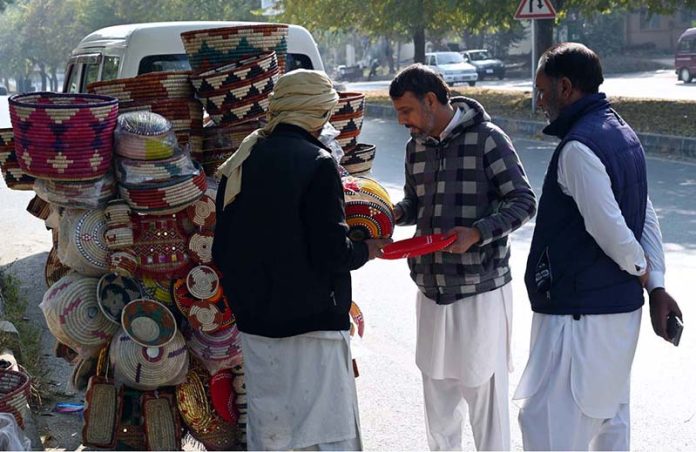 Customers select to purchase colorful handmade household items displayed by a street vendor on the back of his bicycle along a roadside