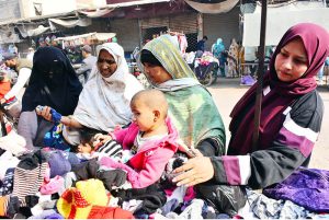 Women busy selecting and purchasing used warm clothes from a vendor during the winter season.