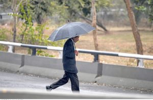 A pedestrian takes shelter under an umbrella walks along the roadside during downpour experienced in the city.
