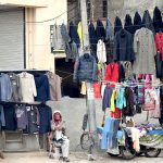 An elderly man displaying second-hand clothes including sweaters waiting for customers at Banni Chowk