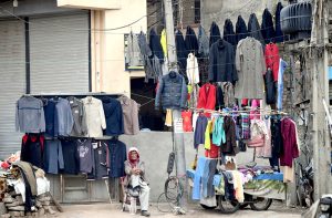 An elderly man displaying second-hand clothes including sweaters waiting for customers at Banni Chowk