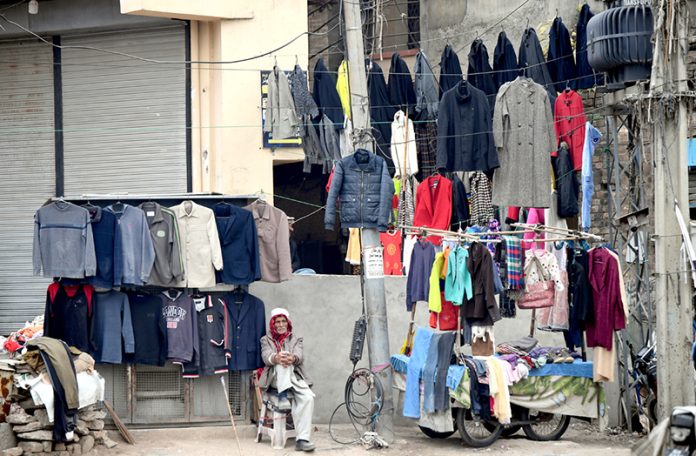 An elderly man displaying second-hand clothes including sweaters waiting for customers at Banni Chowk