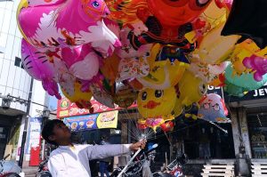 Customers select to purchase colorful handmade household items displayed by a street vendor on the back of his bicycle along a roadside