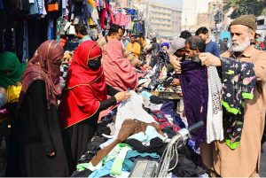 Women busy selecting and purchasing used warm clothes from a vendor during the winter season.