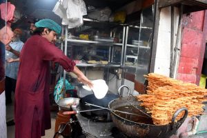 A vendor prepares and displays traditional halwa puri and jalebi at his roadside setup.