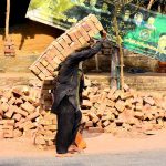 A laborer lifts a heavy bundle of 30 bricks while working on a house construction site in the city.