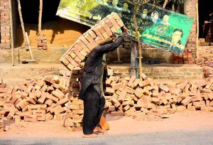 A laborer lifts a heavy bundle of 30 bricks while working on a house construction site in the city.