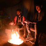 Youngsters sitting around fire to keep warm themselves as the temperature drops rapidly at night time.