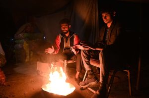 Youngsters sitting around fire to keep warm themselves as the temperature drops rapidly at night time.