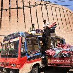 Labourers loading blanket on a passenger bus rooftop at station road.