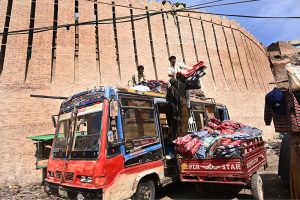 Labourers loading blanket on a passenger bus rooftop at station road.