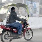 A motorcyclist covers his bike with a plastic shield to protect himself against the cold wind on GT Road.