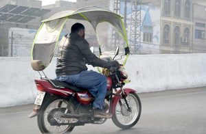 A motorcyclist covers his bike with a plastic shield to protect himself against the cold wind on GT Road.