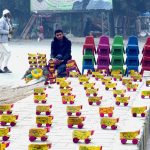 A vendor displays handmade wooden toy trucks while waiting for customers at his roadside setup.