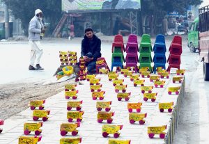 A vendor displays handmade wooden toy trucks while waiting for customers at his roadside setup.