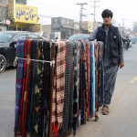 A street vendor pushes a cart laden with colorful woolen scarf along a busy LMQ road attracting customers during the winter season.