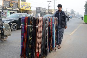 A street vendor pushes a cart laden with colorful woolen scarf along a busy LMQ road attracting customers during the winter season.