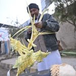 A man stands on College Road making decorative pieces from palm leaves.