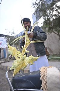 A man stands on College Road making decorative pieces from palm leaves.