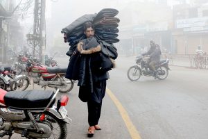 A street vendor carries warm jackets on his shoulders while strolling through the streets for sale at Ghanta Ghar Chowk.